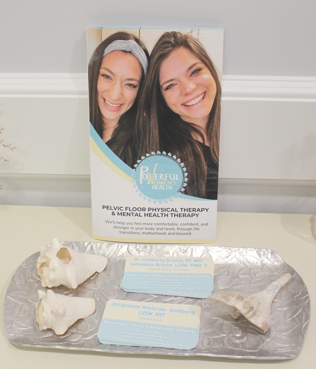 Powerful Women's Health brochure and team business cards on a tray with seashells